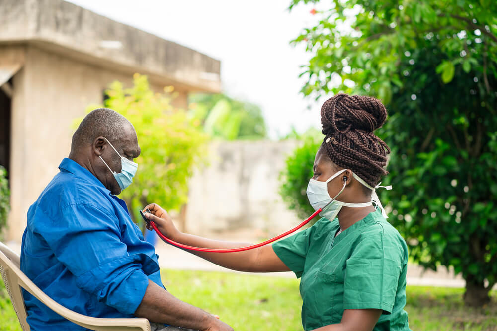 Uma enfermeira negra ouvindo o coração de um paciênte negro com idade aproximada de 65 anos