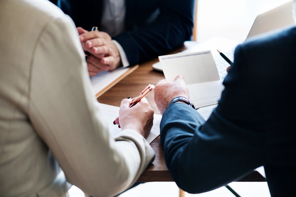 Três pessoas com roupa social analisando documentos, podendo representar advogado(s) e clientes(s) 