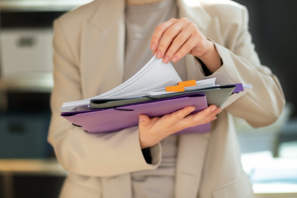mulher com blazer nude carregando pranchetas com documentos do pedido administrado da revisão da vida toda