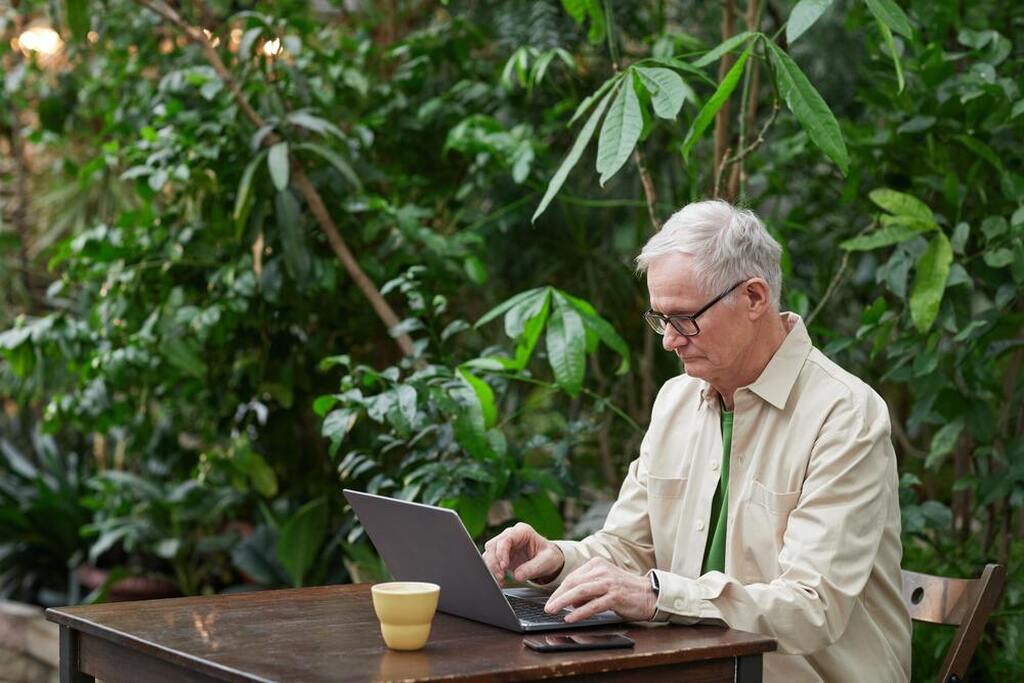 homem ao ar livre sentado em uma mesa de madeira mexendo no computador representando autodeclaração do trabalhador rural