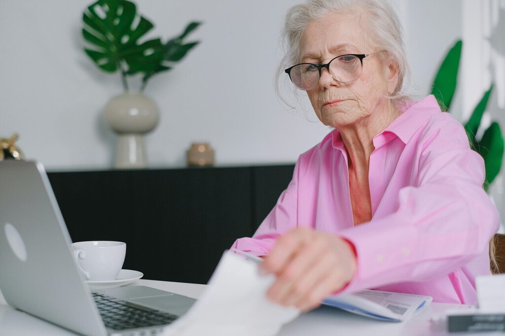 Mulher idosa usando notebook e revisando documentos sobre tipos de aposentadoria.