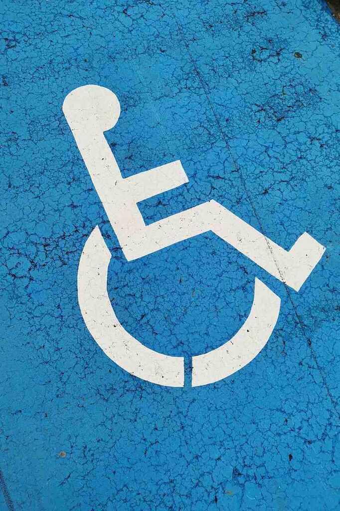 Símbolo de vaga exclusiva para pessoa com deficiência, em branco, sobre chão com tinta azul, representando aposentadoria por idade sem contribuição para pessoas com deficiência.