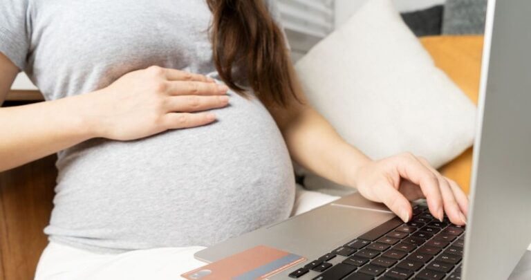 Mulher grávida sentada usando um notebook com um cartão de banco por perto para consultar o salário maternidade aprovado, como receber o benefício no sistema do Meu INSS.