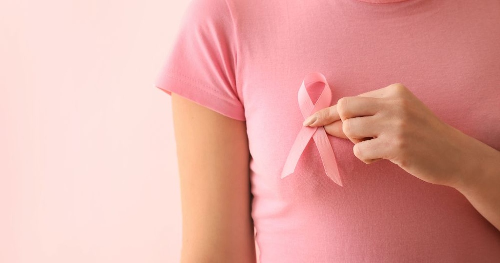 Mulher segurando um laço rosa no peito, simbolizando a conscientização sobre o câncer de mama e a isenção de Imposto de Renda.