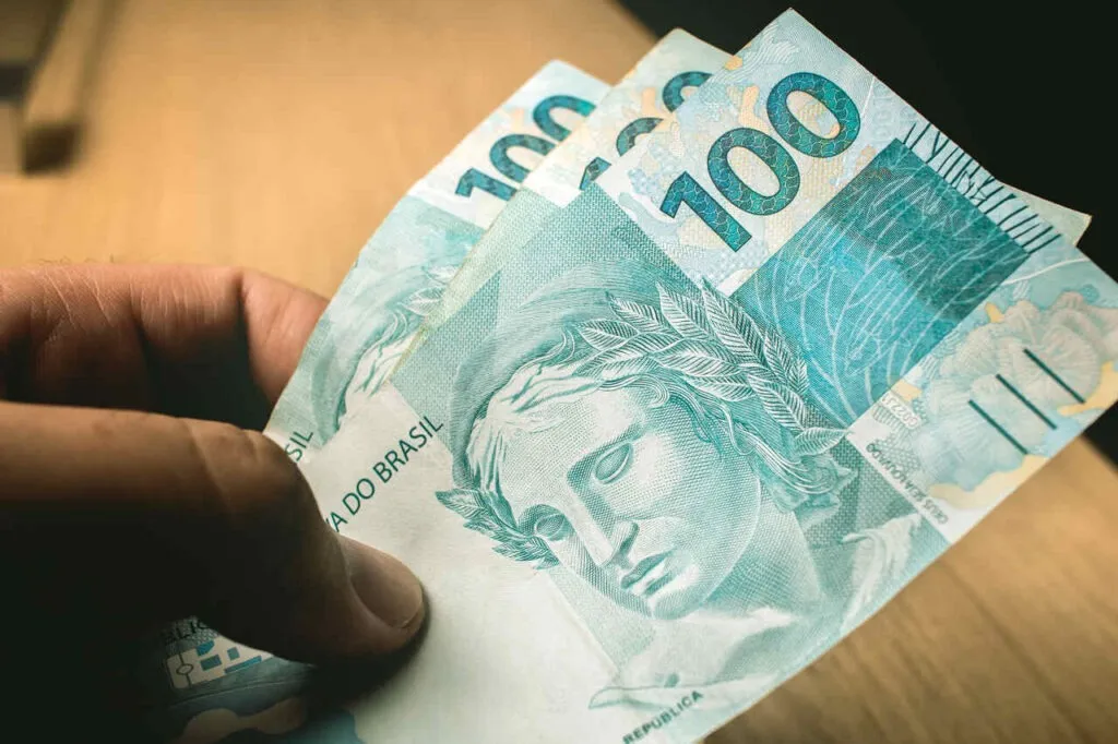 pessoa segurando duas notas de cem reais representando como fica aposentadoria para quem contribuiu antes de 1994